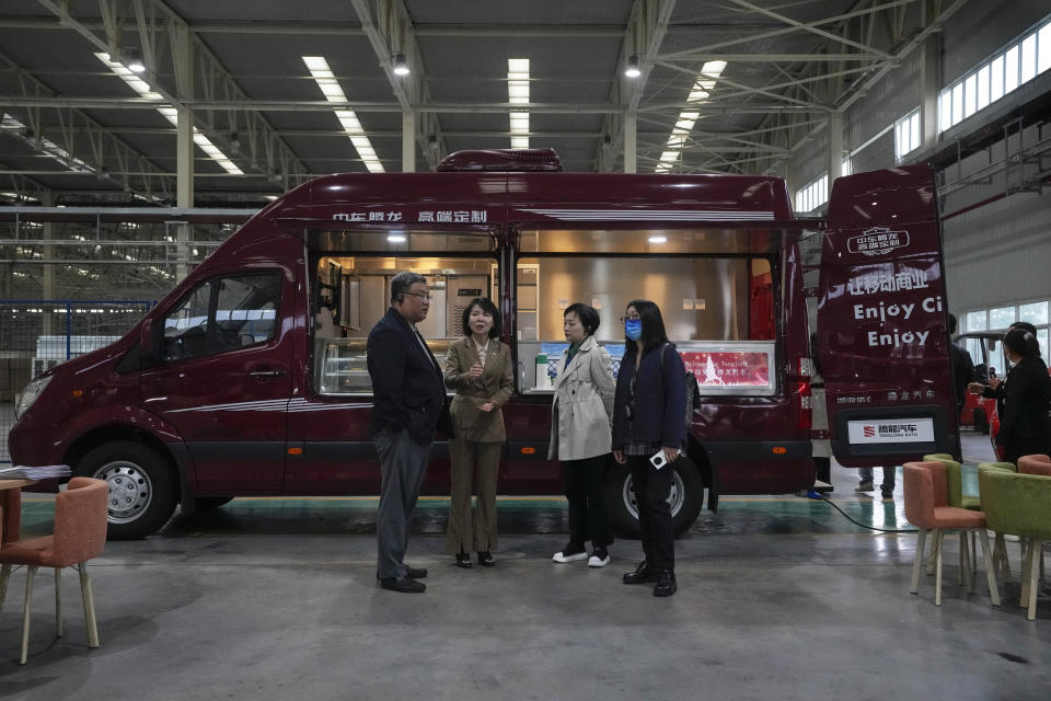 Officials chat near a van converted to a mobile food van at a Tenglong Automobile Co. manufacturing factory during a media-organized tour in Xiangyang in central China's Hubei Province on May 10, 2023. China's manufacturing and consumer spending are weakening after a strong start to 2023 after anti-virus controls ended. (AP Photo/Andy Wong)