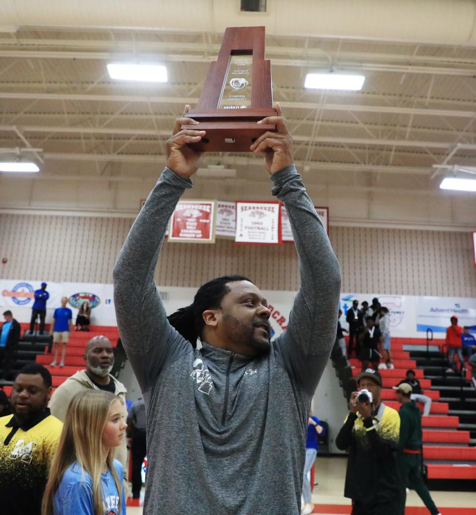 Mainland coach Joe Giddens holds the trophy high after his Bucs beat St. Augustine in the District 4-5A finals at Seabreeze High School on Saturday, Feb. 10, 2024.