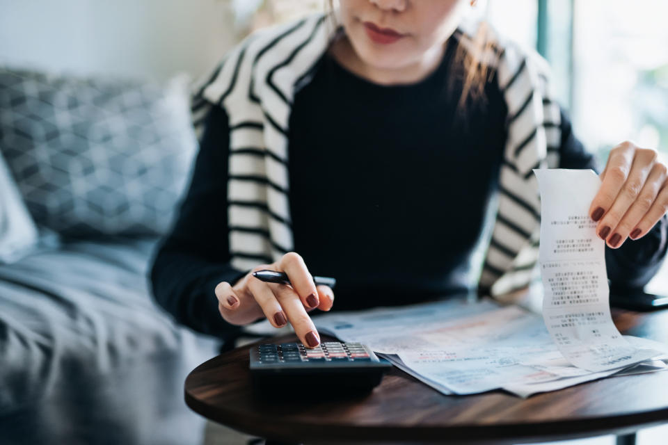 Cropped shot of young Asian woman managing personal banking and finance at home. Planning budget and calculating expenses with calculator. Managing taxes and financial bills. Wealth management. Home budgeting