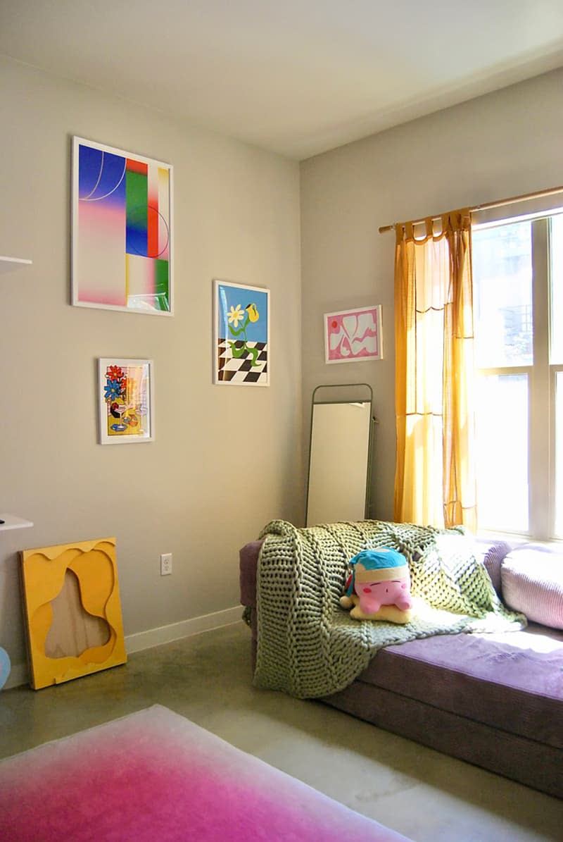 Knitted blanket draped over purple sofa in art filled room.