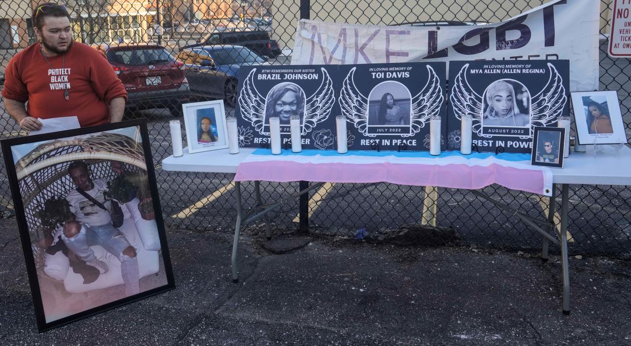 Jaxon Seeger displays photos of transgender women and LGBTQ+ individuals who have died by homicide, during a March 2023 vigil for Cashay Henderson, a transgender woman who was killed.