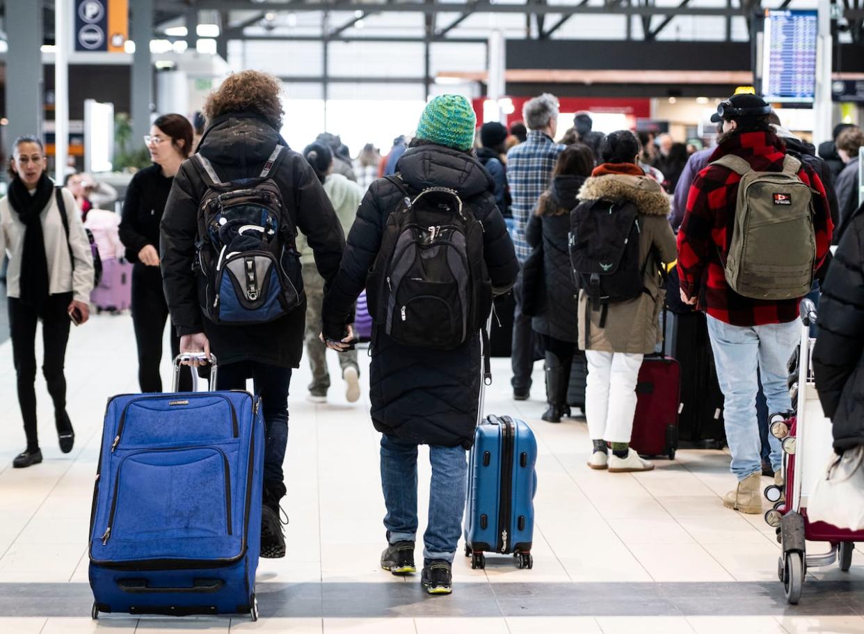 Travellers hold hands as they pass others lining up at the Ottawa International Airport, as airlines cancel or delay flights during a major storm in Ottawa, on Friday, Dec. 23, 2022.  (Justin Tang/The Canadian Press - image credit)