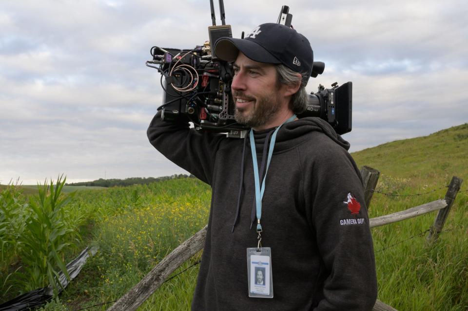 Jason Reitman in a hoodie and baseball cap holding a camera