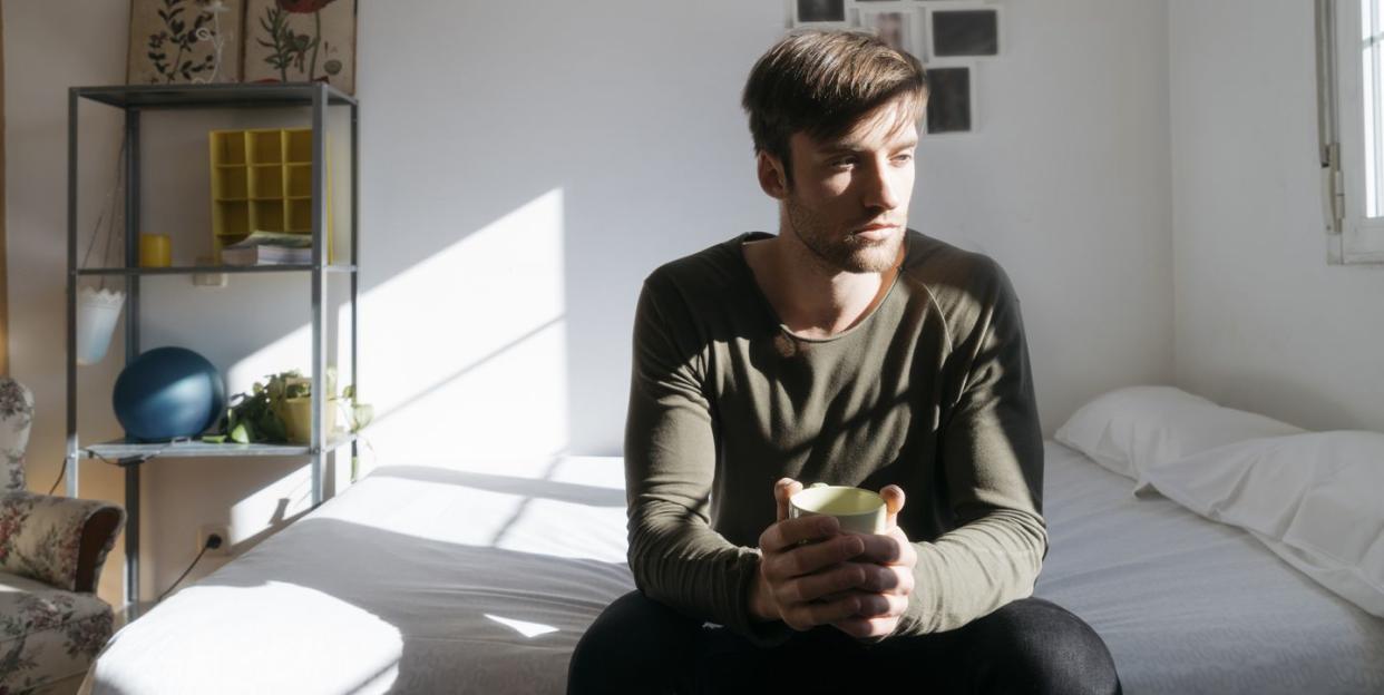 unhappy young man sitting on bed with cup of coffee