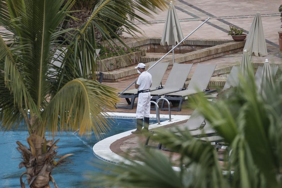 A staffer cleans the swimming pool of the H10 Costa Adeje Palace hotel in La Caleta, in the Canary Island of Tenerife, Spain, Thursday, Feb. 27, 2020. Spanish officials say a tourist hotel on the Canary Island of Tenerife has been placed in quarantine after an Italian doctor staying there tested positive for the COVID-19 virus and Spanish news media says some 1,000 tourists staying at the complex are not allowed to leave. (AP Photo/Joan Mateu)