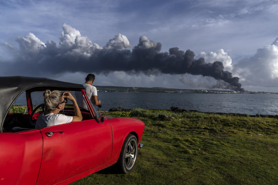 Dos personas observan una columna de humo que se alza desde la base de superpetroleros de Matanzas, Cuba, el 7 de agosto de 2022, donde se desató un incendio letal durante una tormenta eléctrica la noche anterior. (AP Foto/Ramón Espinosa)