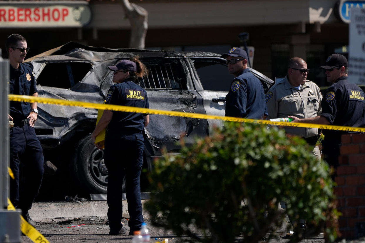 Investigators and police in front of the charred police vehicle (Gregory Bull / AP)