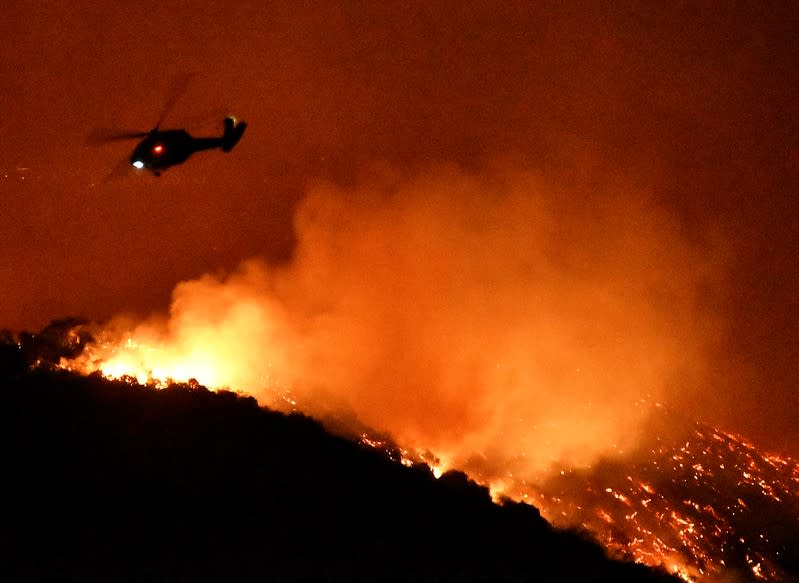 A firefighting helicopter flies over the Getty Fire as it burns in the hills west of the 405 freeway in the hills of West Los Angeles, California