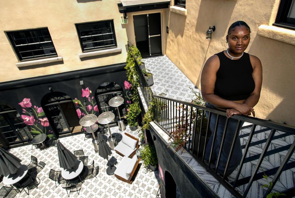 Zahria Eaves stands on a staircase overlooking a courtyard with tables, chairs and flooring with a diamond design pattern.