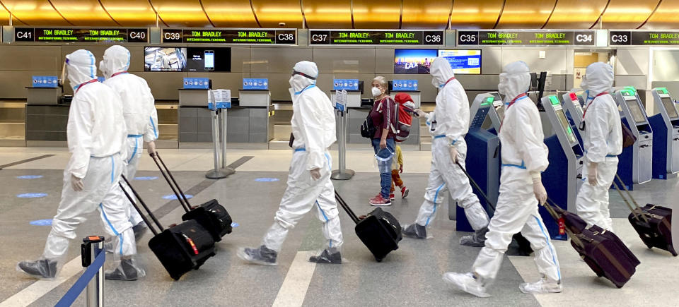 FILE - In this Nov. 17, 2020, file photo, a woman, accompanied by a child, looks over as an airline crew wearing full personal protective equipment against COVID-19, walks through the international terminal at Los Angeles International Airport in Los Angeles. Now, in early May 2021, California has the lowest coronavirus case rate in the country. (Keith Birmingham/The Orange County Register via AP, File)