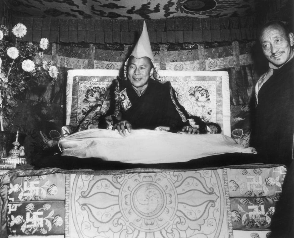 His Holiness the Dalai Lama, Tenzin Gyatso, seated on his throne and wearing the gold peaked cap which is his Crown, smiles while giving an audience in Lhasa, Tibet in 1959.&nbsp;