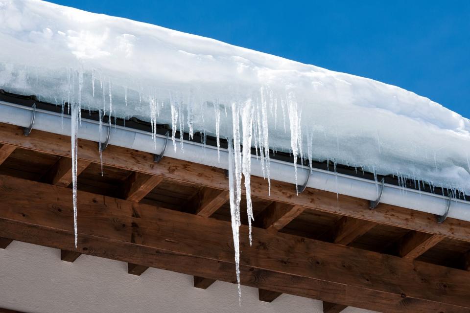 Long icicles and snow overhaning the roof and gutter of a building.