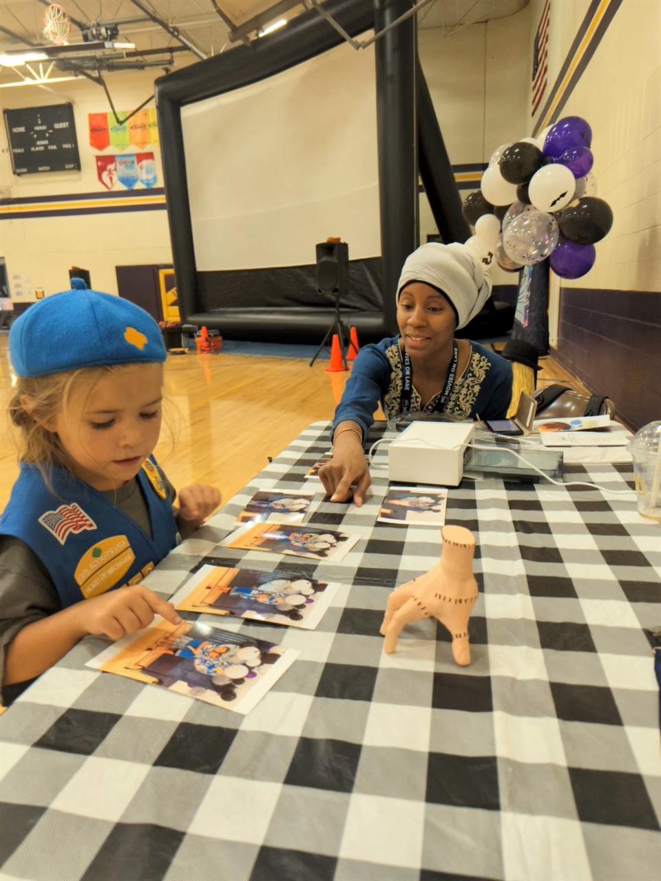 Asia Hawkins, right, Blissfield Community Development Fellow with Community Economic Development Association of Michigan (CEDAM), looks over the "Addams Family" themed photos printed for Eleanor Lowes, 6, of Blissfield during the village's July 20 edition of its Movies on Lane summer programming. Because of inclement weather, all Movies on Lane happenings last week were relocated from downtown Blissfield to the gymnasium at Blissfield Middle School.