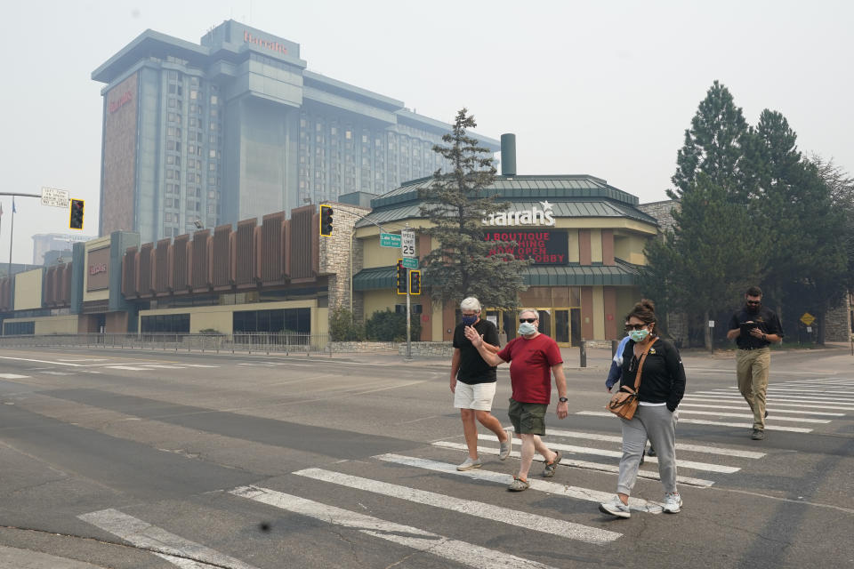 FILE - In this Tuesday, Aug. 24, 2021 file photo, Harrah's Lake Tahoe Casino is shrouded in smoke as face mask wearing pedestrians cross the street at the California-Nevada line. Last week, managers overseeing the fight against the massive wildfire scorching California's Lake Tahoe region thought they could have it contained by the start of this week. Instead, on Monday, Aug. 30, 2021, the Caldor Fire crested the Sierra Nevada, forcing the unprecedented evacuation of all 22,000 residents of South Lake Tahoe. (AP Photo/Rich Pedroncelli, File)