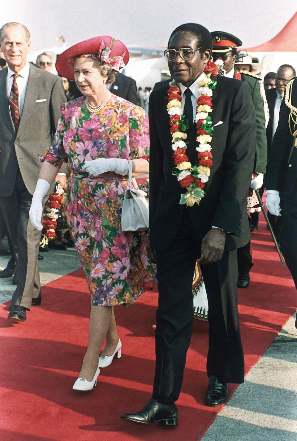 FILE - Britain's Queen Elizabeth II is escorted by Zimbabwean President Robert Mugabe, right, after the Queen's arrival at Harare airport on a second visit to the country, Oct. 10, 1991. After seven decades on the throne, Queen Elizabeth II is widely viewed in the U.K. as a rock in turbulent times. But in Britain’s former colonies, many see her as an anchor to an imperial past whose damage still lingers. (AP Photo/Gill Allen, File)