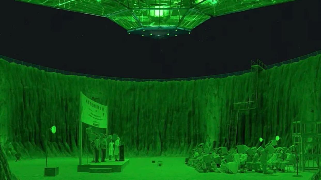  tables and chairs are set up in a crater bathed in green light 