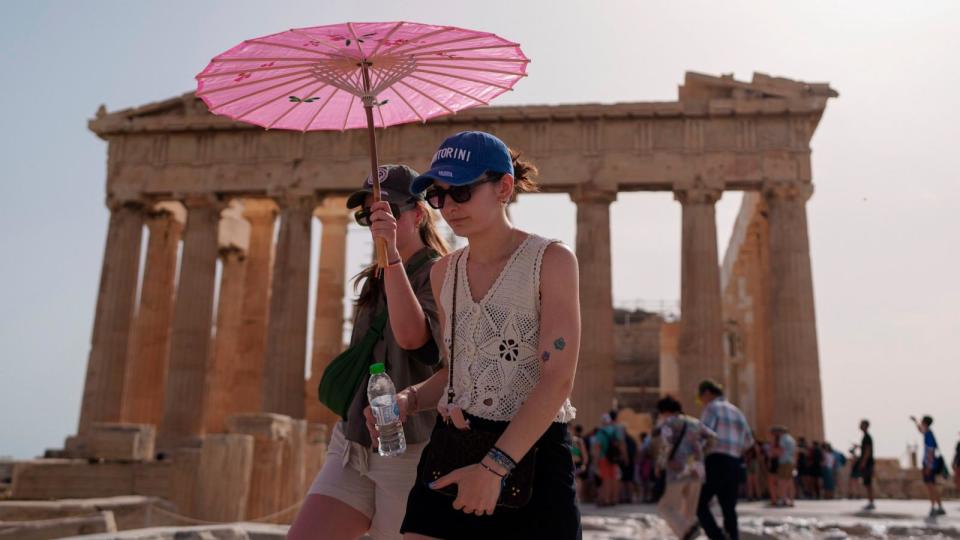 PHOTO: Tourists with an umbrella walk in front of the 5 century BC Parthenon at the ancient Acropolis before it was closed in Athens, June 12, 2024.  (Petros Giannakouris/AP)