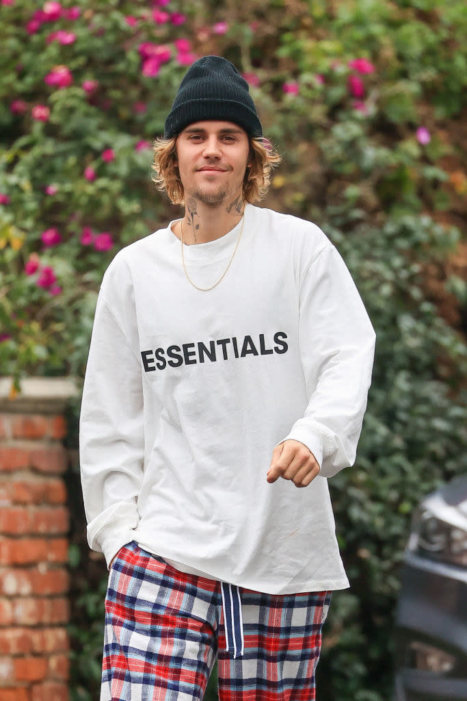 Justin smiling and walking outside in a shirt that says Essentials on the front