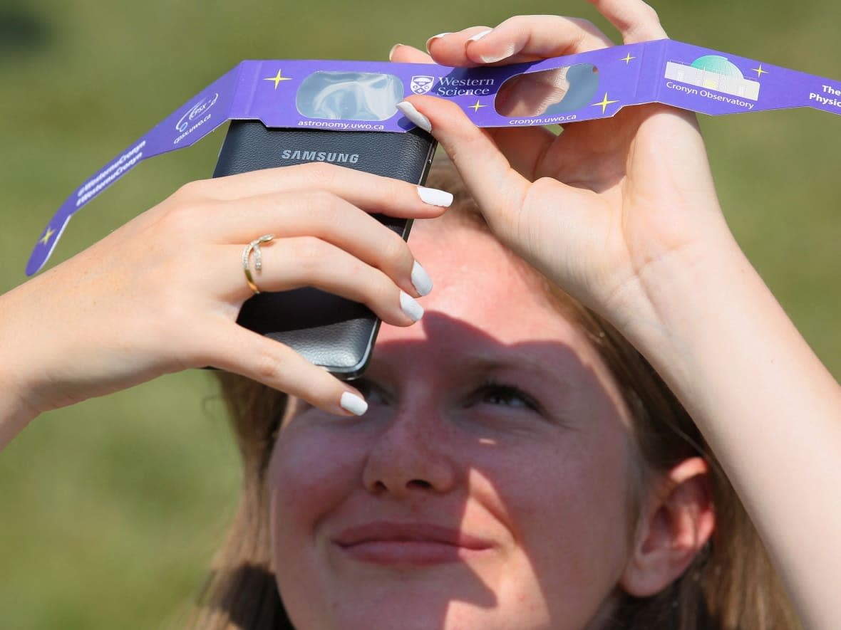 Mélanie Meinrad holds solar glasses over her phone to take a photo of the partial solar eclipse on Aug. 21, 2017, in London, Ont. To avoid frying your phone while trying to capture the upcoming total solar eclipse, photographers recommend covering the lens with a solar filter like the one in eclipse glasses.  (Dave Chidley/The Canadian Press - image credit)