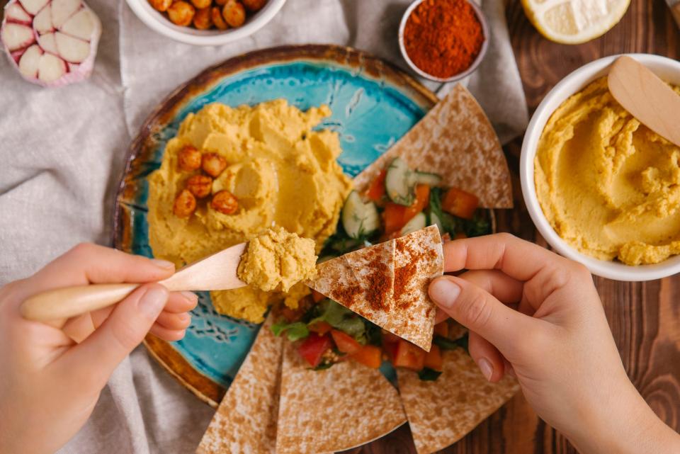 a close up of a pair of hands spreading hummus on pita bread