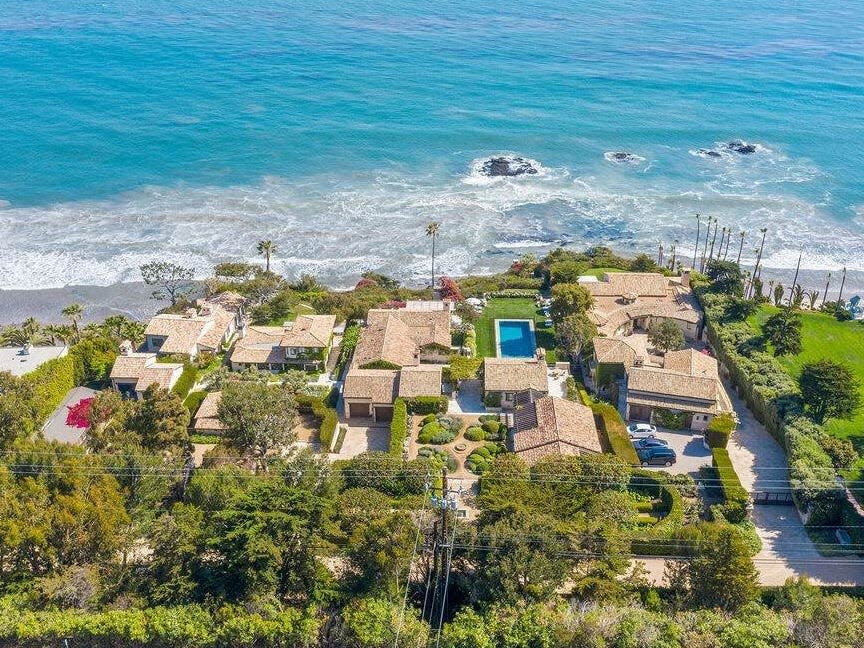 a sprawling home surrounded by trees on one side and the ocean on the other in California