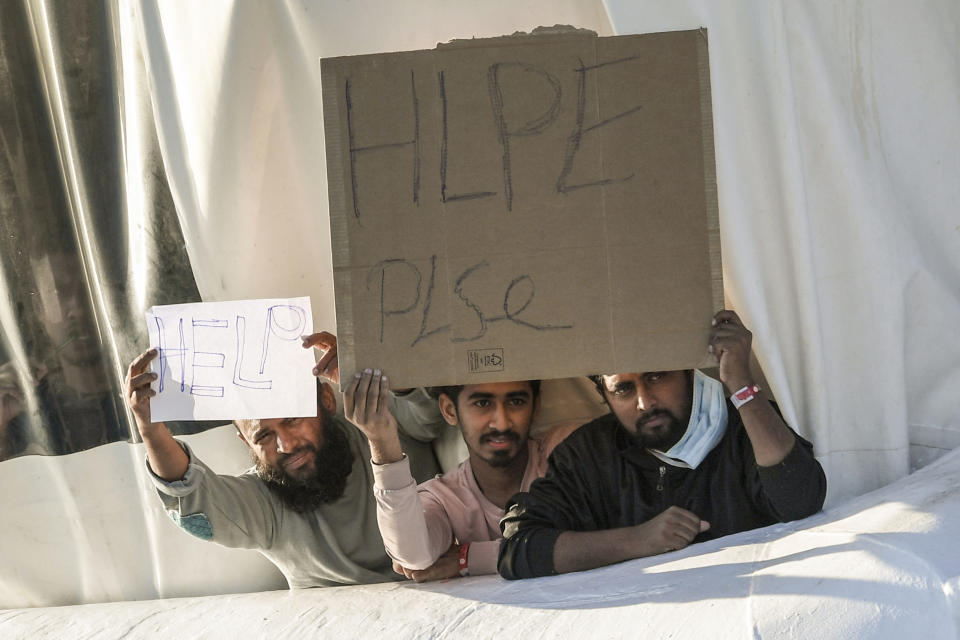 Migrants hold banners asking for help, from a deck of the Norway-flagged Geo Barents ship operated by Doctors Without Borders, in Catania's port, Sicily, southern Italy, Monday, Oct. 7, 2022. The Geo Barents has been allowed Sunday to disembark 357 migrant that Italian authorities defined as "vulnerable people" and minors, while leaving another 215 people that were declared non-vulnerable blocked on board. (AP Photo/Salvatore Cavalli)