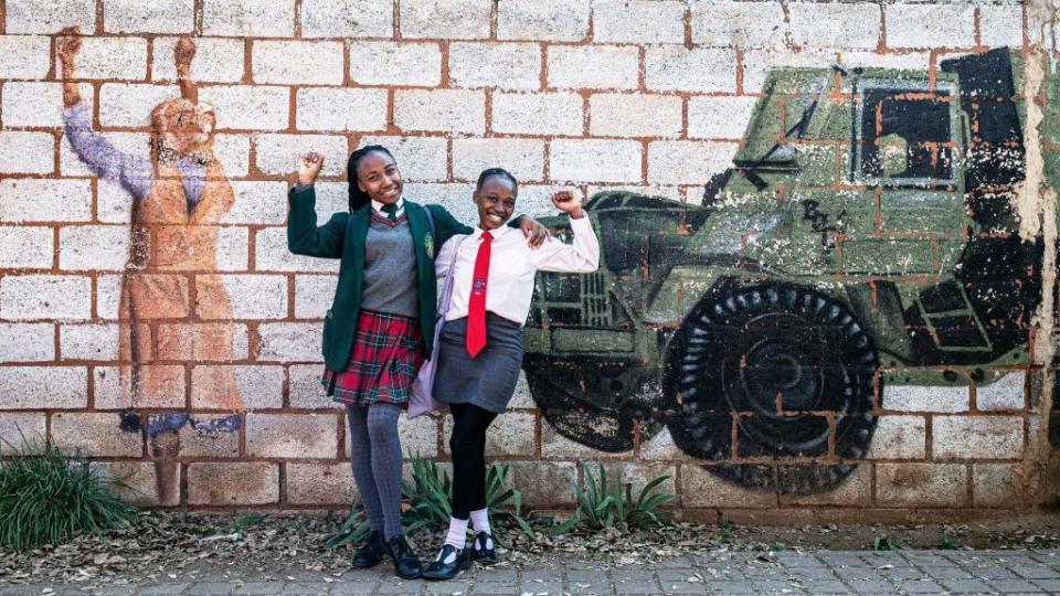 Girls pose for pictures at a mural after visiting the Hector Pieterson Museum on June 16, 2024 in Soweto, South Africa. The Soweto Uprising began on June 16, 1976, as a peaceful student protest against the enforcement of Afrikaans in schools. The police and army's response with tear gas and bullets led to violent clashes, resulting in the deaths of 400 to 700 people, many of them children. The event galvanized international opposition to apartheid and is commemorated annually in South Africa as Youth Day.