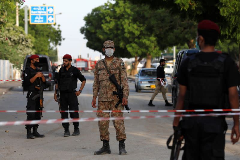 Army soldier and police officers guard a cordoned-off street leading to the site of a passenger plane crash in a residential area near an airport in Karachi,