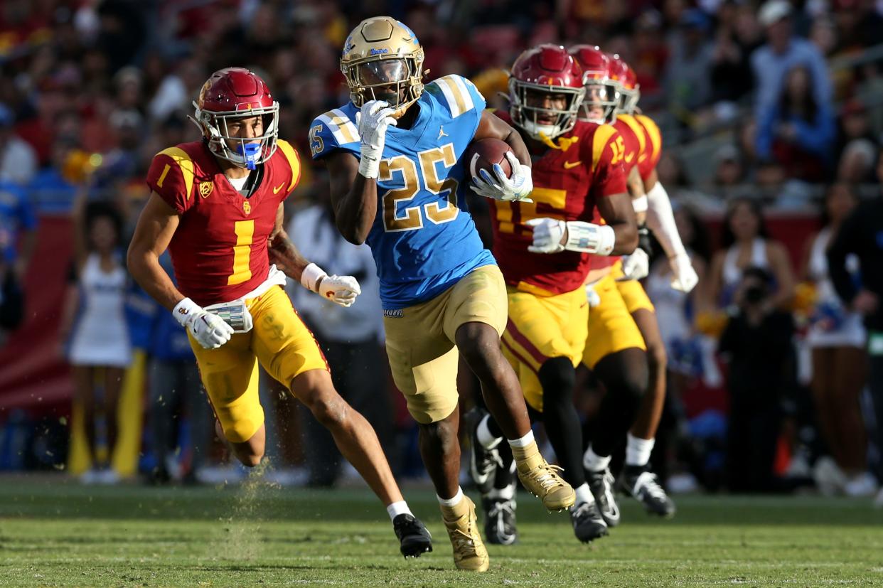 UCLA Bruins running back TJ Harden (25) runs against USC Trojans cornerback Domani Jackson (1) and safety Anthony Beavers Jr. (15) during the third quarter at United Airlines Field at Los Angeles Memorial Coliseum on Nov. 18 in Los Angeles.