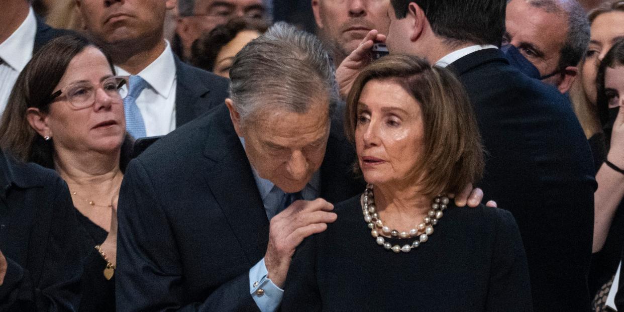 Paul Pelosi touches Nancy Pelosi's shoulder.