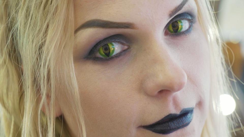 Close-up portrait of young pretty woman with halloween makeup at beauty salon. Face of lady with cat eyes contact lenses.