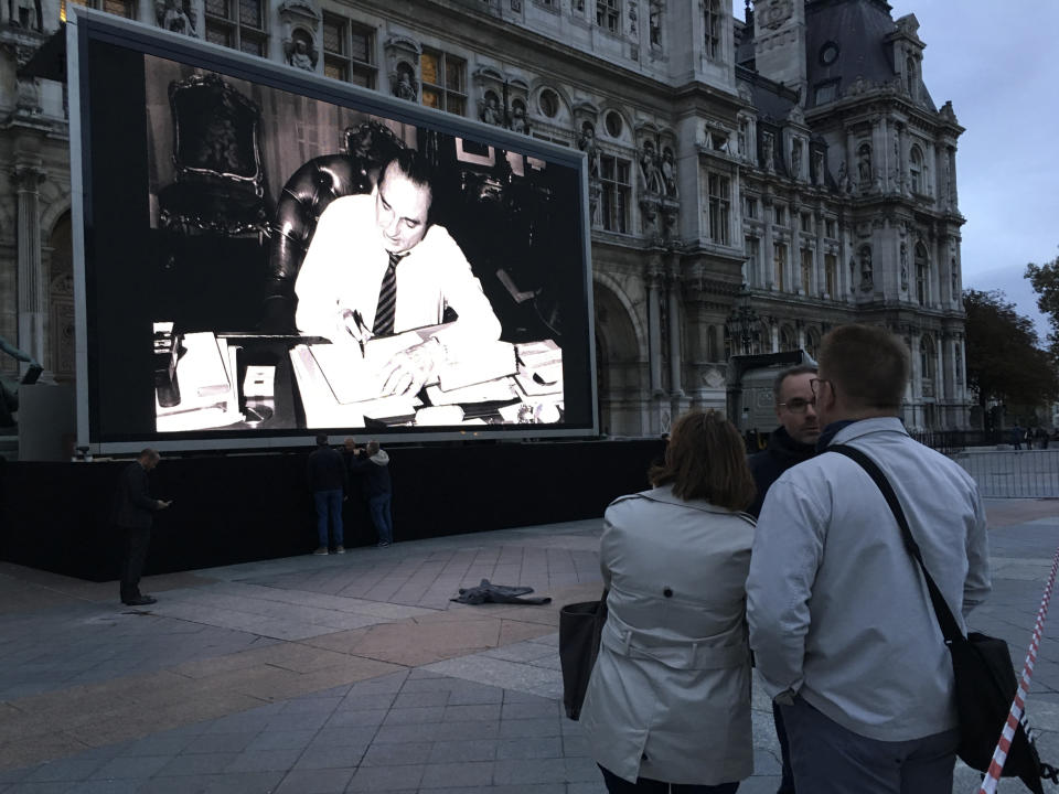 People watch former President Jacques Chirac on a giant screen set up at the Paris town hall, Thursday, Sept. 26, 2019 in Paris. Jacques Chirac, a two-term French president who was the first leader to acknowledge France's role in the Holocaust and defiantly opposed the U.S. invasion of Iraq in 2003, has died at age 86. (AP Photo/Alexander Turnbull)