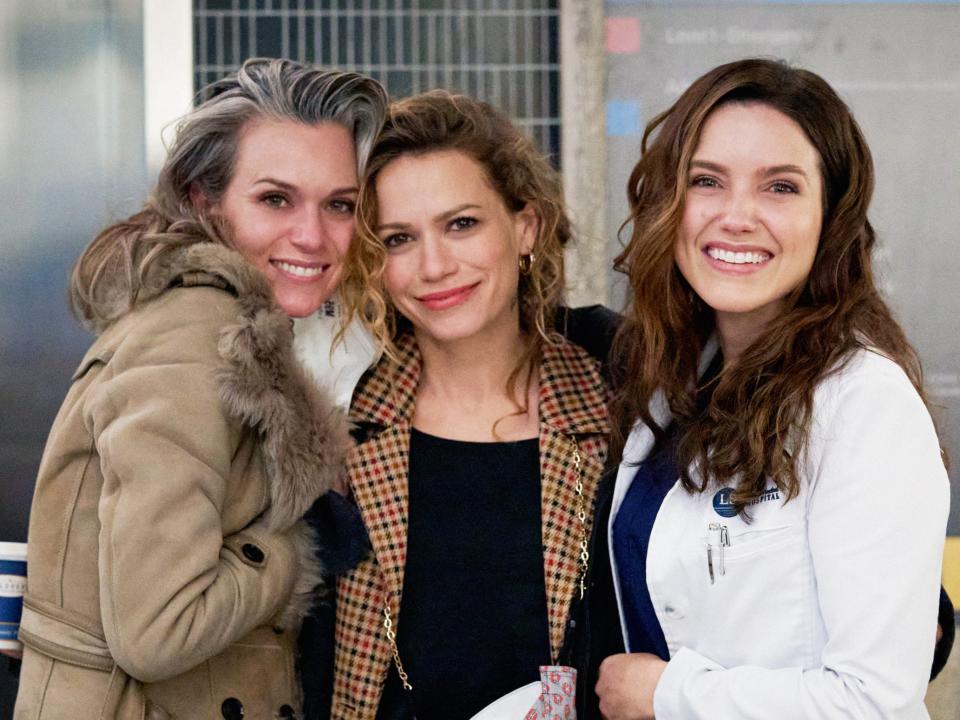 Three women dressed in character in ordinary clothes Sophia in a doctor's coat. They're all smiling and hugging.