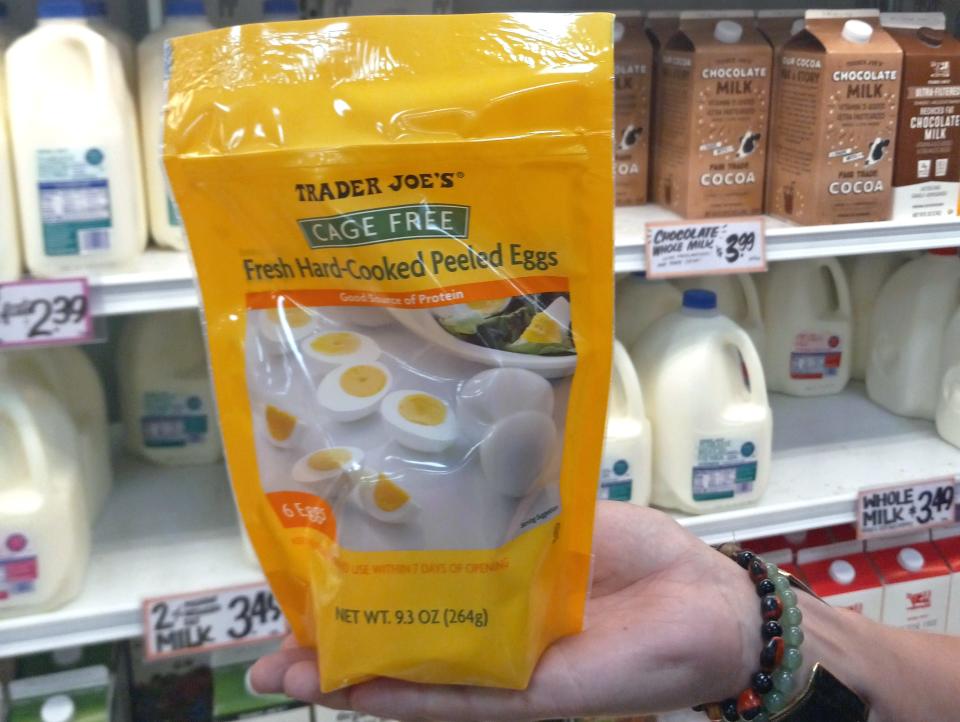 hand holding package of hard boiled eggs in front of the dairy case at trader joes