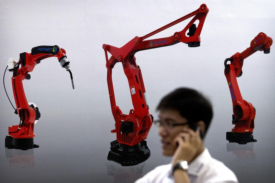 FILE - In this Aug. 15, 2018, file photo, a visitor talks on his phone in front of a display of manufacturing robots from Chinese robot maker Honyen at the World Robot Conference in Beijing, China. Two surveys show Chinese factory activity grew in April but below the previous month's pace amid a tariff battle with Washington. (AP Photo/Mark Schiefelbein, File)