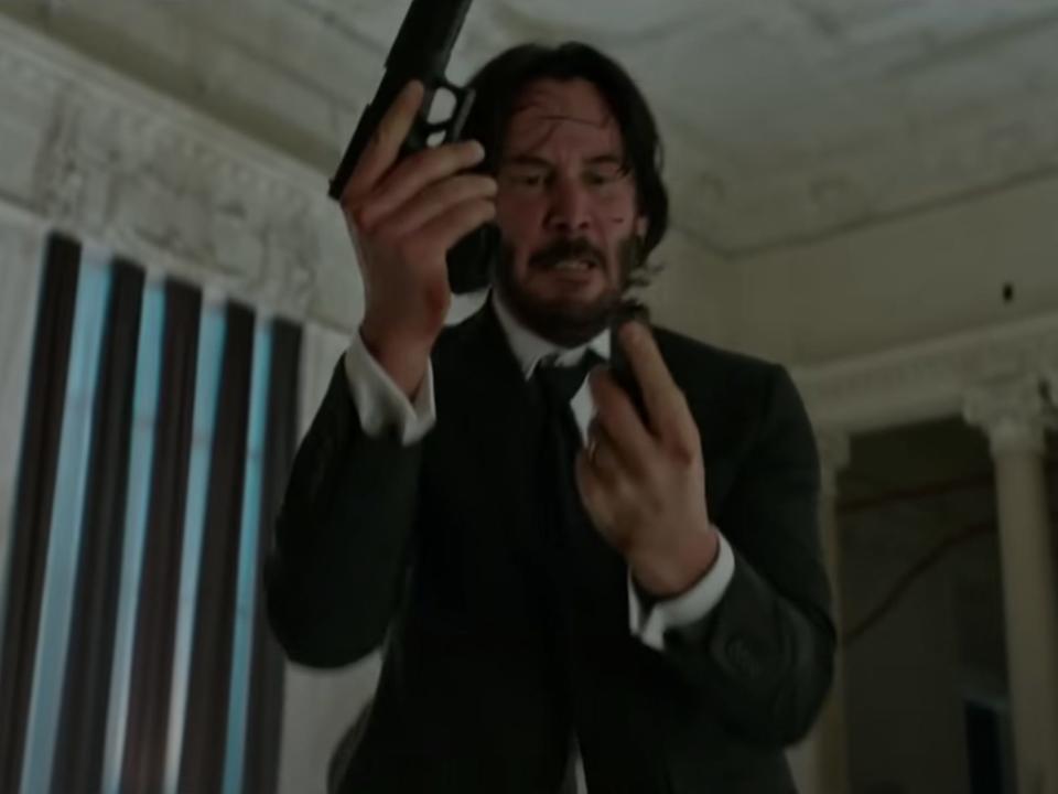 Keanu Reeves as John Wick reloading his gun in a museum.