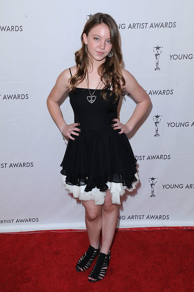 Young female celebrity posing at the Young Artist Awards in a knee-length black dress with layered skirt and strappy heels