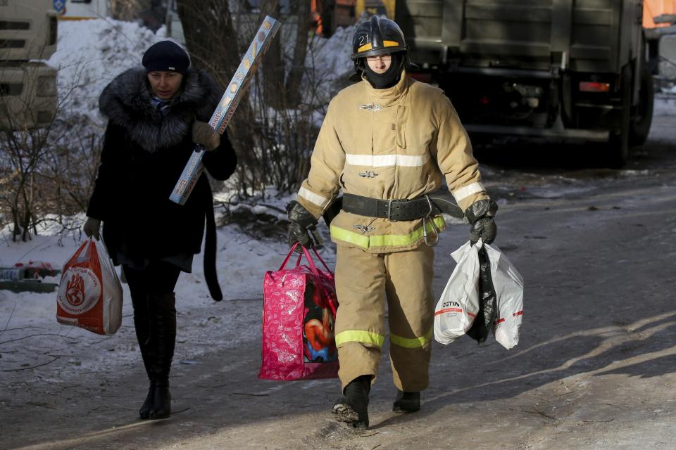 An Emergency Situations employee helps a woman to carry her goods from apartments located near the destroyed part a collapsed apartment building in Magnitogorsk, a city of 400,000 people, about 1,400 kilometers (870 miles) southeast of Moscow, Russia, Wednesday, Jan. 2, 2019. Search crews have pulled more bodies from a huge pile of rubble at a collapsed Russian apartment building. The building's pre-dawn collapse on Monday came after an explosion that was believed to have been caused by a gas leak. (AP Photo/Maxim Shmakov)
