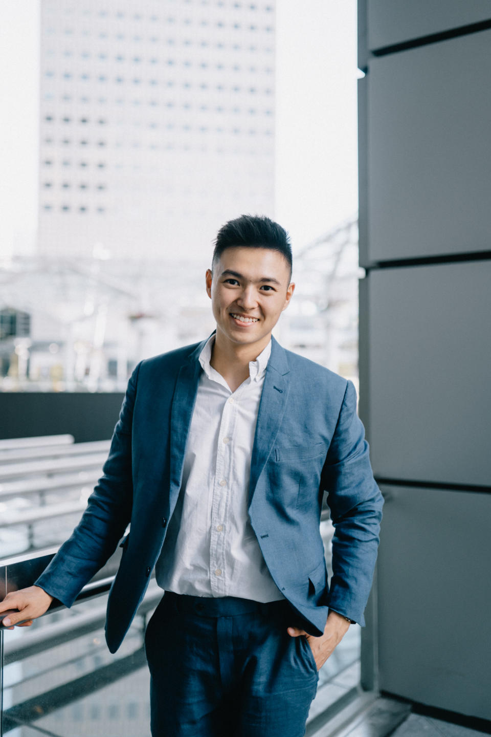 Damien Tan photographed in a casual suit against a backdrop of office buildings, illustrating a story on how he managed to buy two private condos by the time he turned 24.