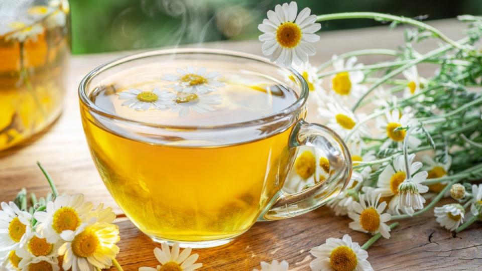 A mug of chamomile tea beside chamomile flowers