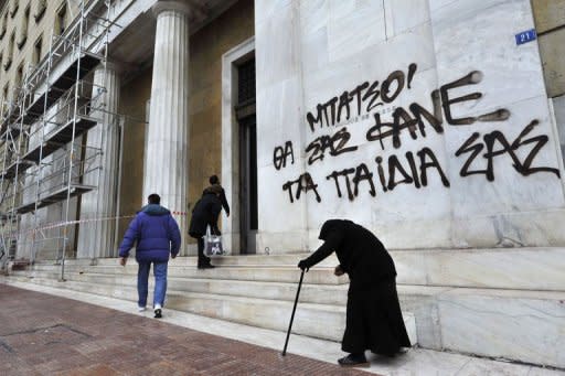 An eldery woman begs by the Bank of Greece headquarters in Athens. Eurozone finance ministers put a new Greek bailout on hold after Athens failed to meet conditions demanded by lenders in return for a rescue package it desperately needs to avoid default