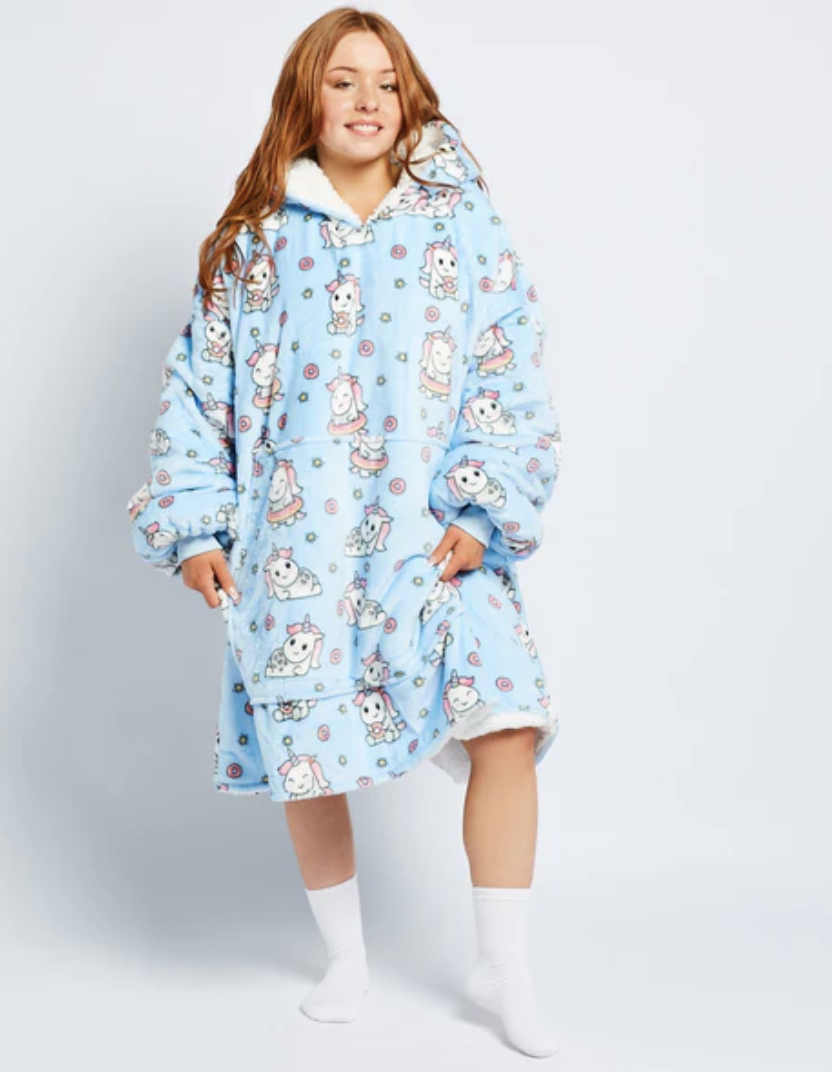 A girl stands in a sky blue Oodie featuring cute cartoon unicorn prints