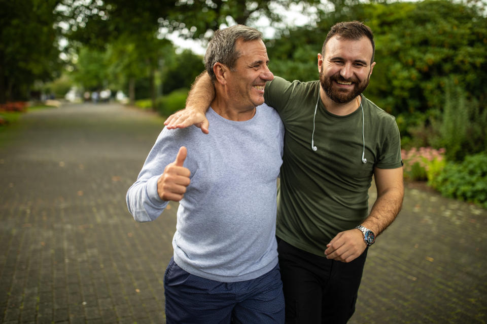 Mature gray-haired man and his son jogging and embracing in public park on autumn morning