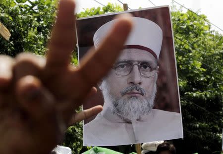 A supporter gestures in front of a picture of Muhammad Tahirul Qadri, Sufi cleric and leader of political party Pakistan Awami Tehreek (PAT) as they begin their march toward the capital from Lahore August 14, 2014. REUTERS/Mohsin Raza