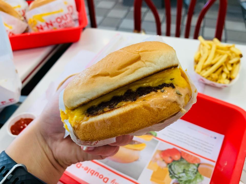 hand holding in-n-out cheese burger in front of white tables with red trays