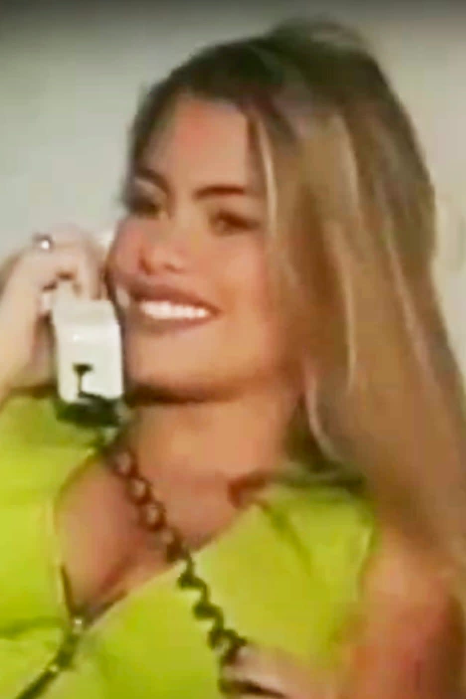 Sofía Vergara, smiling and talking on a corded phone, wears a sleeveless, zip-front top