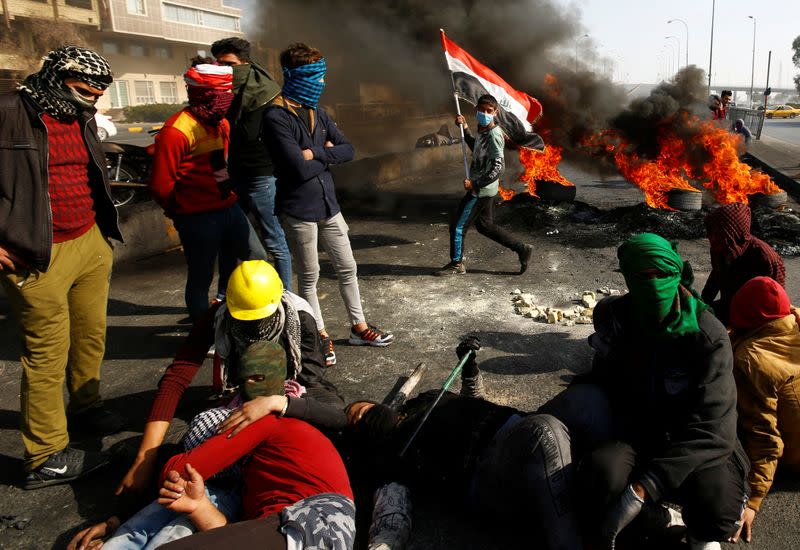 Iraqi demonstrators sit on the street near burning tires blocking a road during ongoing anti-government protests in Najaf