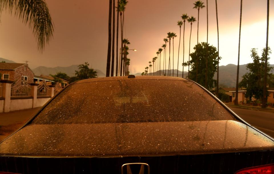 Ash falls on a parked car as the Bobcat fire burns in the distance