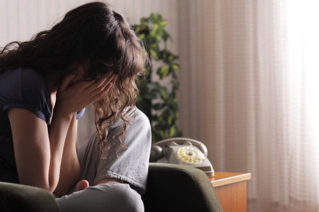 Depressed young woman sitting in chair at home