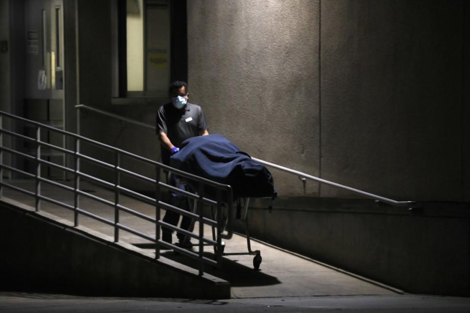 A worker wheels a stretcher with a deceased patient